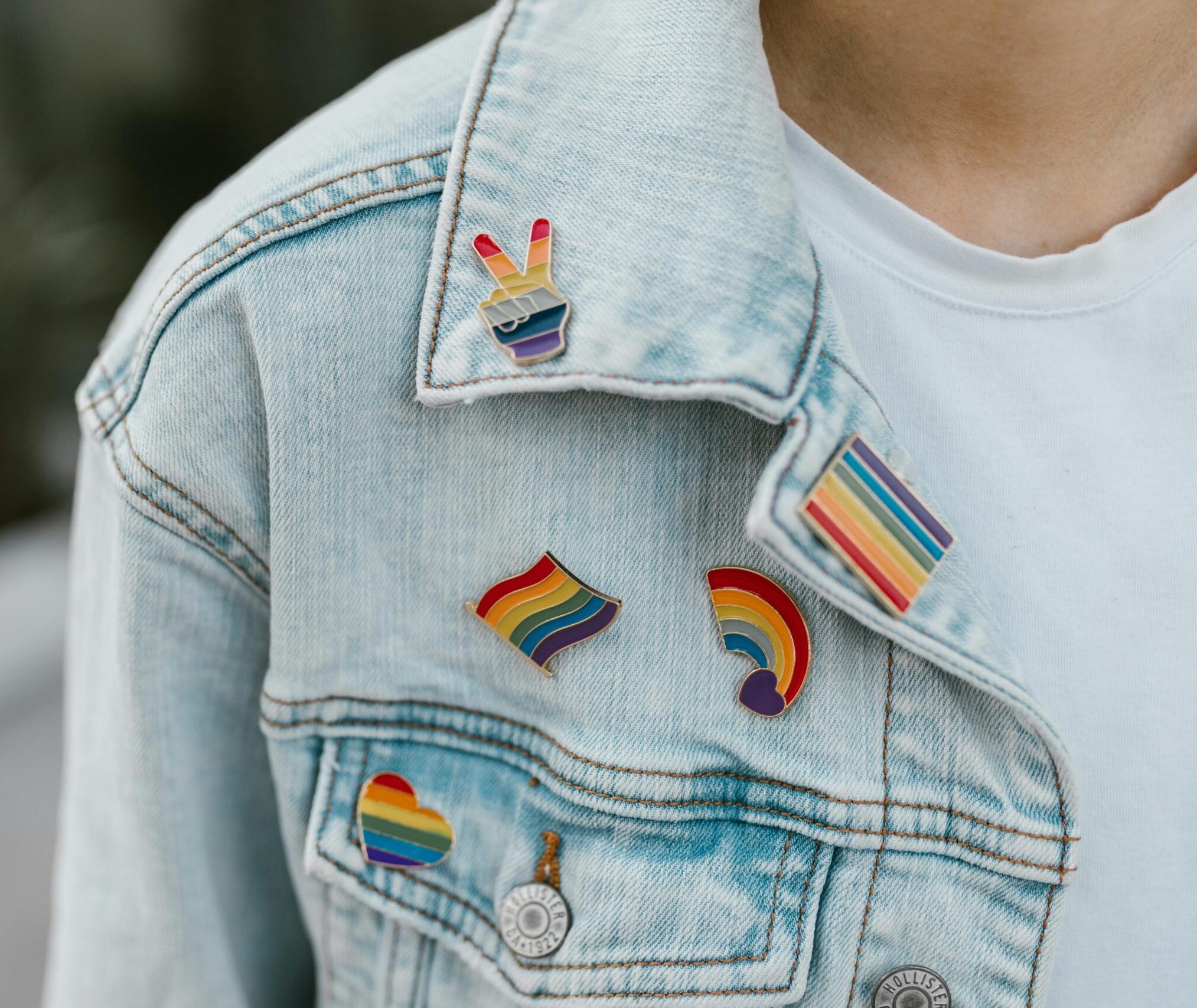A denim jacket with several rainbow-design pins.