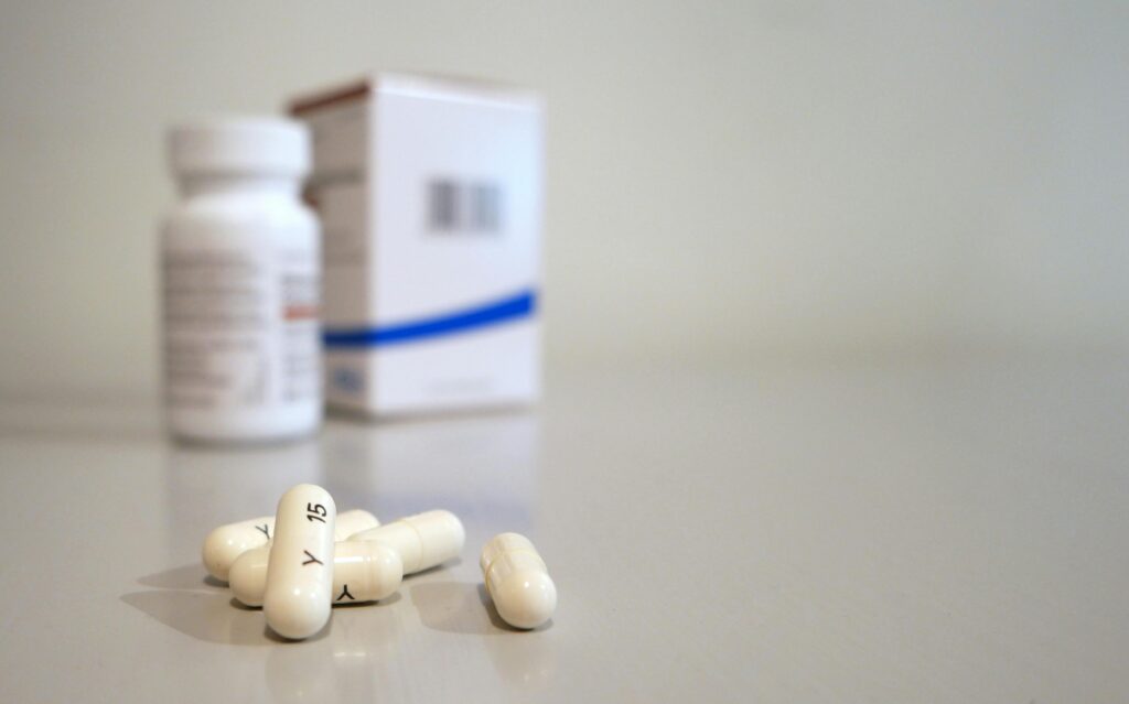 Various pills sit on a table in front of a white pill bottle and a white box.